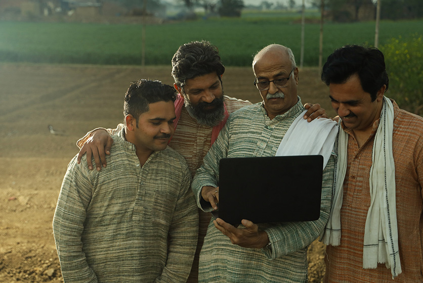 Farmers gathered in a field looking at a laptop