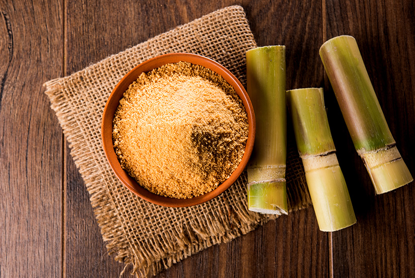 Wooden bowl with jaggery powder next to sugarcane pieces